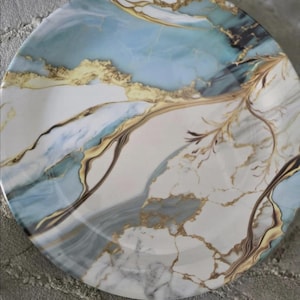 Puede incluir: Un plato redondo con un patrón de mármol en tonos blanco, azul claro y azul oscuro, acentuado con vetas doradas intrincadas que crean un diseño orgánico y ramificado en la superficie de esta pieza de vajilla de cerámica.