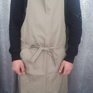 May include: A beige apron with adjustable straps and a tie at the waist. The apron is made of a durable fabric and has a simple design.