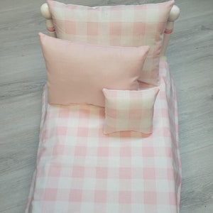 Puede incluir: Una cama en miniatura con ropa de cama de cuadros rosas y blancos y tres almohadas. Las almohadas son de diferentes tamaños y tonos de rosa. El marco de la cama es blanco con detalles en rosa, creando una estética encantadora y acogedora.