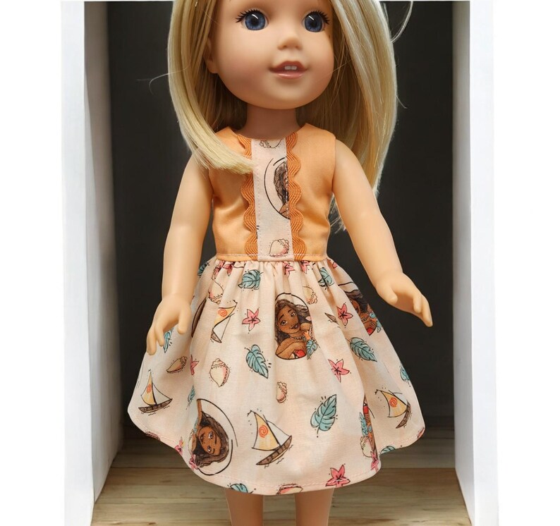 Puede incluir: Una mu&ntilde;eca con un vestido color melocot&oacute;n con estampado floral. El vestido presenta un corpi&ntilde;o sin mangas y una falda acampanada. La falda est&aacute; adornada con ilustraciones de un personaje, veleros y hojas tropicales. La mu&ntilde;eca tiene cabello rubio y ojos azules.