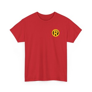Könnte beinhalten: Rotes T-Shirt mit gelbem Kreis und schwarzem "R"-Logo auf der Brust. Das T-Shirt hat kurze Ärmel und ist aus weichem Stoff. Das Design ist schlicht und auffällig, mit einem kräftigen Farbschema.