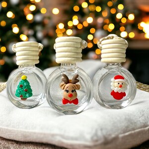 以下が含まれることがあります： 白い木製の蓋と吊り下げ用の紐が付いたガラス製の車の芳香剤が3つあります。芳香剤は透明な液体で満たされており、クリスマスのテーマになっています。1つの芳香剤は緑色のクリスマスツリー、もう1つは赤いトナカイ、そしてもう1つは赤いサンタクロースです。