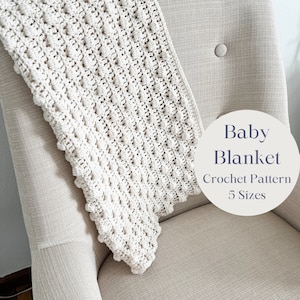 May include: A white crocheted baby blanket with a textured bobble stitch pattern, draped over a chair. The text "Baby Blanket Crochet Pattern 5 Sizes" is on a white circle.