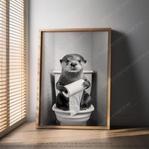 May include: A black and white photo of an otter sitting on a toilet holding a roll of toilet paper. The otter is looking directly at the camera.