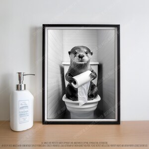 May include: A black and white photo of an otter sitting on a toilet holding a roll of toilet paper. The otter is looking directly at the camera.