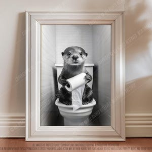 May include: A black and white photo of an otter sitting on a toilet holding a roll of toilet paper. The otter is looking at the camera.