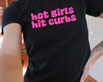 Op de afbeelding: Zwart T-shirt met de tekst "hot girls hit curbs" in roze bubbelletters.