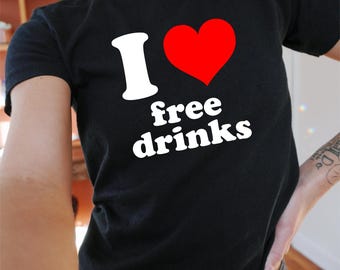 Op de afbeelding: Zwart T-shirt met de tekst "I ❤️ free drinks" in wit en rood. Het shirt heeft een ronde hals. De persoon draagt ook een donkerblauwe jeans.