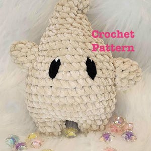 Könnte beinhalten: Ein beiges, plüschiges, sternförmiges Häkelspielzeug mit zwei schwarzen ovalen Augen und einer spitzen Oberseite. Der Text "Crochet Pattern" ist in Pink auf der rechten Seite aufgedruckt. Mehrere kleine, durchscheinende, bunte Sternperlen liegen davor.