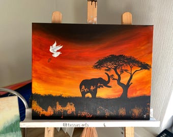 May include: A painting of a sunset with a silhouette of an elephant and a tree. A white dove flies in the sky above the elephant. The painting is on a canvas and is framed.