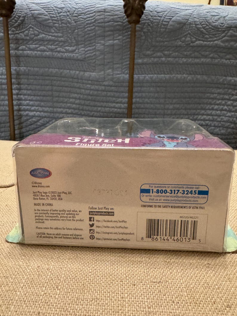 以下が含まれることがあります： スティッチのフィギュアセットが入った青と紫の箱。箱の前面にはディズニーのロゴと「スティッチフィギュアセット」の文字が書かれている。箱の裏面には、製造元、ウェブサイト、安全に関する情報など、製品に関する情報が記載されている。バーコードは箱の裏面に表示されている。