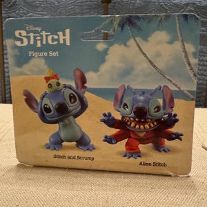以下が含まれることがあります： ディズニーのスティッチのフィギュアセット。スティッチとスクランプ、大きな耳を持つ青い宇宙人と、脅迫的な表情をした赤い宇宙人のスティッチがいます。パッケージには、ヤシの木と青い空の熱帯の背景が描かれています。