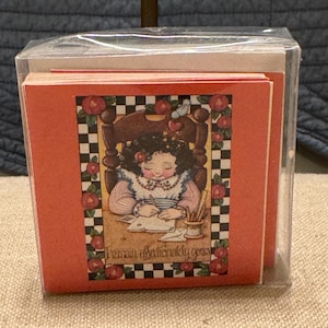 May include: A set of red note cards with a black and white checkered border. The cards feature a cartoon illustration of a girl sitting in a chair writing a letter. The text on the card reads "I remain affectionately yours".