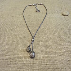 May include: A silver-toned lariat necklace featuring a delicate woven chain and two dangling spherical charms. The charms are encrusted with small, clear, reflective stones. The necklace includes a lobster claw clasp and an adjustable extender chain.