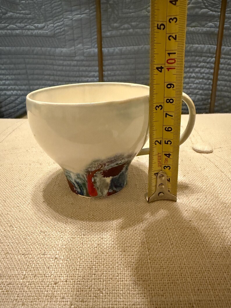 May include: A white ceramic mug with a black handle and the text "But First, Coffee" in a bold, black font. The mug is set against a blurred background, suggesting a cozy setting.
