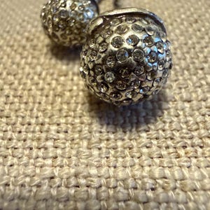 May include: Two spherical cufflinks featuring a silver-toned metal base densely encrusted with numerous small, clear, faceted crystals. The surface of each cufflink has a textured, multi-faceted appearance created by the embedded stones.
