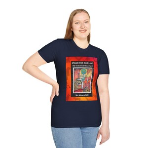 May include: A navy blue short-sleeve t-shirt featuring a rectangular graphic with an orange and red gradient background. The graphic displays the text "STAND FOR OUR LAND", "NO Industrial Wind Here!", and "No Means NO!" alongside a colorful illustration.