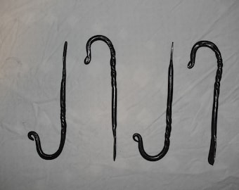 Può includere: Quattro ganci in metallo nero con un design attorcigliato. I ganci sono lunghi circa 25 cm e hanno una forma semplice e curva.