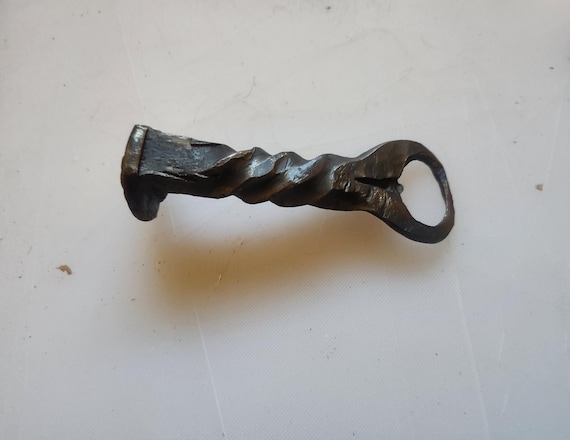 An actual railroad spike, hand-twisted and hammer-forged by a blacksmith into a bottle opener — functional industrial sculpture with a story behind every swing.
