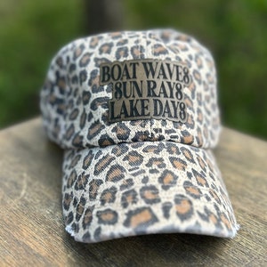 May include: A brown and white leopard print baseball cap with a brown patch that says "BOAT WAVE SUN RAYS LAKE DAYS" in black letters.