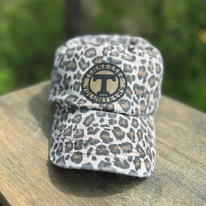 May include: A brown and black leopard print baseball cap with a gold and black circular patch that says "Tennessee Volunteers" with a large "T" in the center.