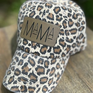 May include: A brown and white leopard print baseball cap with a brown leather patch that says "MAMA" in black lettering.