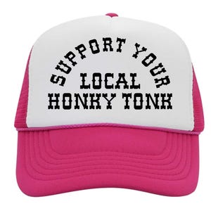 May include: A trucker hat with a white front panel and a hot pink brim and mesh back. The hat features the text "SUPPORT YOUR LOCAL HONKY TONK" in black, arched across the front.