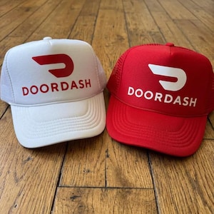 May include: Two trucker hats, one white with a red DoorDash logo and text, and one red with a white DoorDash logo and text. Both hats feature a structured front panel, a curved brim, and a mesh back panel, displaying the brand name clearly.