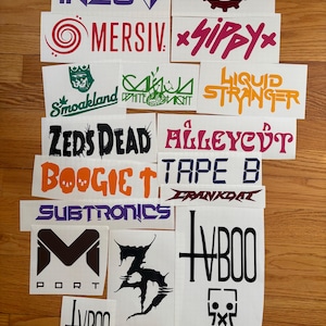 Puede incluir: Una colección de pegatinas blancas con varios logotipos y textos. Las pegatinas presentan nombres como "INZO", "CRANKDAT", "MERSIV", "SippY", "Smoakland", "ZEDS DEAD", "ALLEYCUT", "BOOGIE", "SUBTRONICS" e "IVBOO", en varios colores y fuentes.