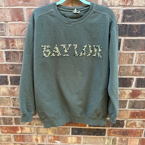 Op de afbeelding: Een groen sweatshirt met het woord "BAYLOR" geborduurd in groen en geel op de voorkant.