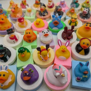 May include: A selection of novelty rubber ducks, each with a unique design. The ducks are displayed on small, rectangular and circular platforms. The designs include a snowman, reindeer, and bunny, with a variety of bright colours.