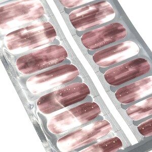 May include: A pack of nail polish wraps with a brown and white ombre design with gold glitter accents.