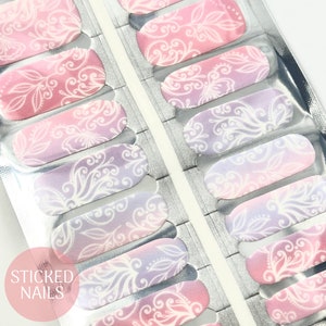 Op de afbeelding: Een set nagelwraps met een wit bloemenpatroon op een roze en paarse ombre-achtergrond. De nagelwraps zijn verpakt in een doorzichtige plastic hoes met de tekst "STICKED NAILS" gedrukt in de linkerbenedenhoek.