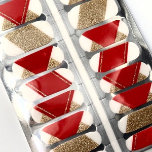 Op de afbeelding: Een vel met rode en gouden nagellak wraps met een geometrisch ontwerp. De wraps zijn verpakt in een zilveren foliezakje.