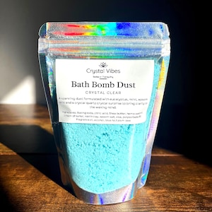 Può includere: Busta olografica piena di polvere blu per bombe da bagno. L'etichetta recita "Crystal Vibes Bath Bomb Dust CRYSTAL CLEAR" con un elenco di ingredienti. Il prodotto è formulato con eucalipto, menta e sali di Epsom.