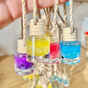May include: Five small glass bottles with colorful glitter inside, hanging from a string with wooden tops. The bottles are purple, yellow, red, blue, and clear.