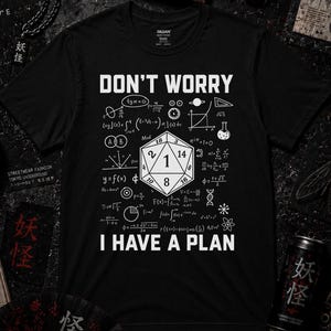 Può includere: Una t-shirt nera a maniche corte con una stampa grafica bianca di un dado a venti facce circondato da varie formule matematiche e il testo "DON'T WORRY I HAVE A PLAN" centrato sul davanti con un girocollo.