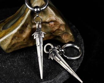 Könnte beinhalten: Ein Paar silberfarbene Creolen mit einem hängenden schwertförmigen Anhänger. Die Ohrringe haben eine polierte metallische Oberfläche mit einem spitz zulaufenden Klingendesign und einem kleinen Ringverbinder an einem Klappverschluss.