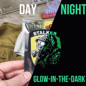 Può includere: Una toppa che brilla al buio con un teschio stilizzato che indossa una maschera antigas. La toppa è gialla, verde e nera e ha il testo "STALKER" su di essa.