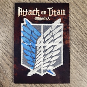May include: A grey, white and blue embroidered patch with the text "Attack on Titan" and Japanese characters. The patch features a winged symbol with a grey background.