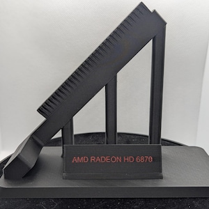May include: Black plastic stand with three legs and a sloping top. The stand has the text "AMD Radeon HD 6870" printed on the front.