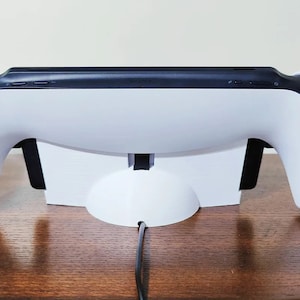 May include: White Nintendo Switch console with black Joy-Con controllers attached to the console, sitting on a white charging stand with a black cable.