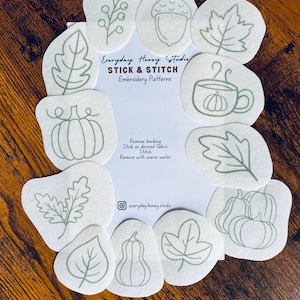 May include: A collection of white Stick & Stitch embroidery patterns featuring fall-themed designs. The patterns include leaves, pumpkins, acorns, and a cup of tea with a pumpkin. The text "Everyday Honey Studio" and "STICK & STITCH Embroidery Patterns" is visible.