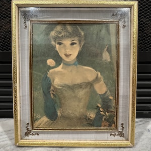 May include: A framed vintage print of a woman in a light blue dress holding a white flower. The woman has dark hair and is wearing a blue ribbon around her neck. The print is in a gold and white frame with a decorative border.