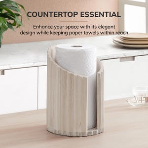 Peut inclure: Un porte-essuie-tout cylindrique en bois clair avec une texture nervur&eacute;e verticale et une large ouverture frontale. Le support contient un rouleau d'essuie-tout blanc. Le texte au-dessus indique : COUNTERTOP ESSENTIAL. Enhance your space with its elegant design while keeping paper towels within reach.