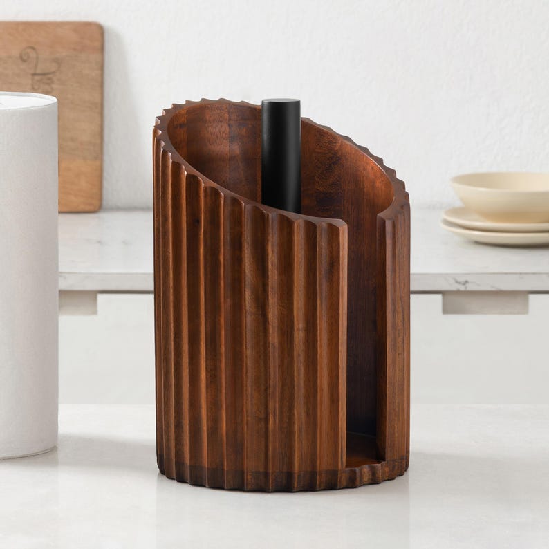 Peut inclure: Un porte-essuie-tout cylindrique en bois brun fonc&eacute; avec une texture cannel&eacute;e verticale. Le support comprend une tige centrale en m&eacute;tal noir mat pour maintenir le rouleau, avec une ouverture frontale pour un acc&egrave;s facile.