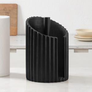 Peut inclure: Un porte-essuie-tout noir mat au design cylindrique avec des cannelures verticales et une tige centrale droite. La structure pr&eacute;sente une silhouette incurv&eacute;e ouverte sur le devant, offrant une base solide pour les rouleaux de papier essuie-tout.