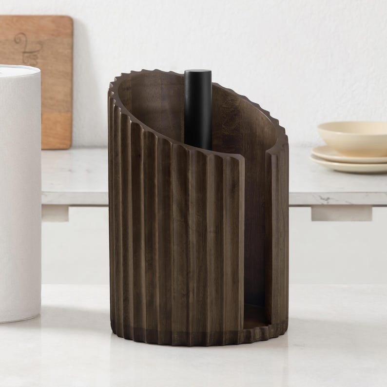 Peut inclure: Un porte-essuie-tout cylindrique marron fonc&eacute; avec une texture cannel&eacute;e verticale sur l'ext&eacute;rieur. Le support pr&eacute;sente une large fente verticale ouverte sur le devant et une tige centrale noire solide s'&eacute;levant de la base pour fixer le rouleau.