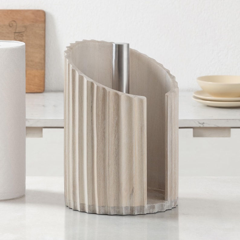 Peut inclure: Un porte-essuie-tout cylindrique dot&eacute; d'un ext&eacute;rieur en bois cannel&eacute; beige clair avec des rainures verticales et une tige centrale en m&eacute;tal argent&eacute;. La structure pr&eacute;sente une large ouverture verticale sur un c&ocirc;t&eacute; pour ins&eacute;rer le rouleau.