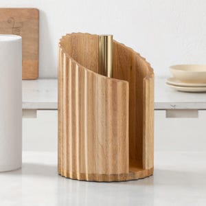 Peut inclure: Un porte-essuie-tout cylindrique en bois dot&eacute; d'une texture cannel&eacute;e verticale et d'une tige centrale en m&eacute;tal dor&eacute;. Le support pr&eacute;sente une conception ouverte sur le c&ocirc;t&eacute;, mettant en valeur le grain du bois clair naturel et une base arrondie.